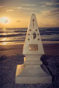 A monument on the beach with a sunset in the background.