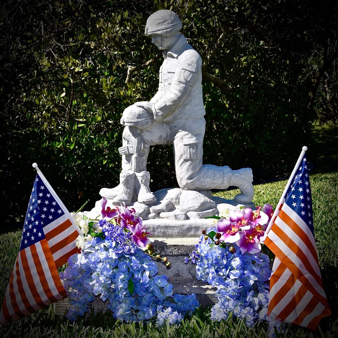 A statue of a soldier kneeling down in front of two american flags.