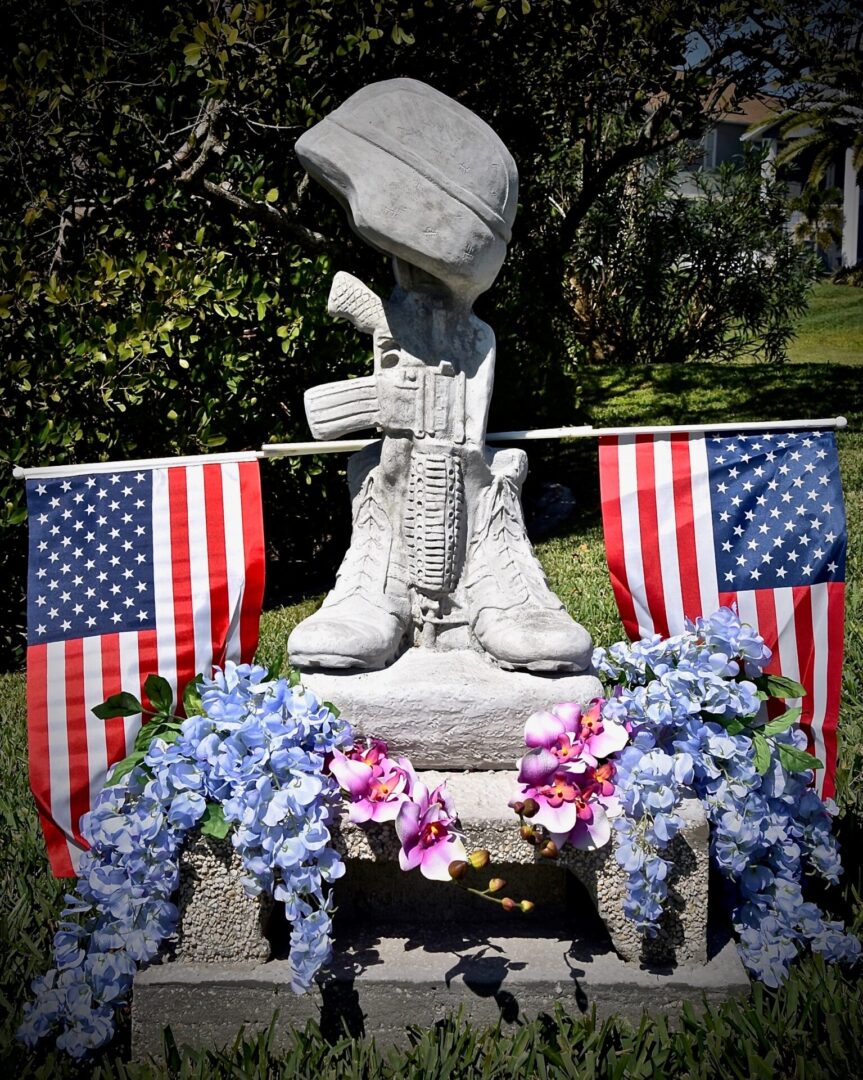 A statue of a soldier with flowers and american flags.